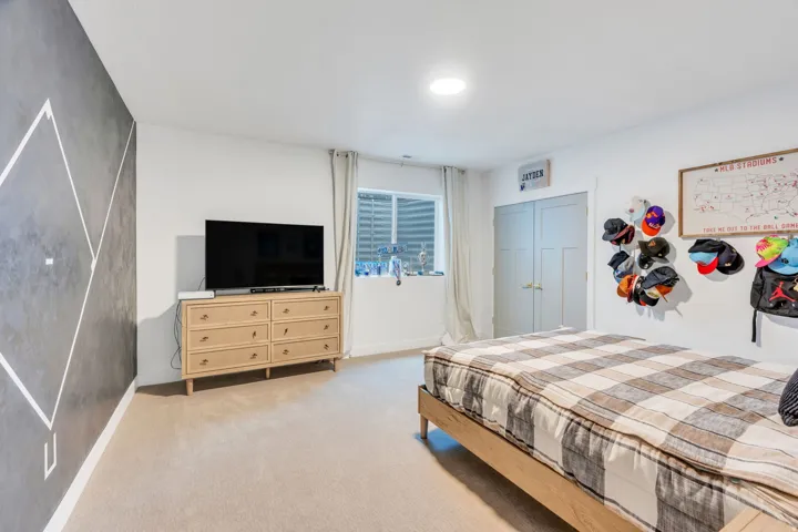 Bedroom featuring neutral carpet flooring, a geometric accent wall, and a window with white blinds
