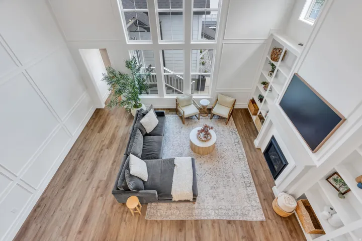 Two-story living area featuring tall windows with grid patterns, wood-finish flooring, a fireplace with integrated shelving, and white wall paneling