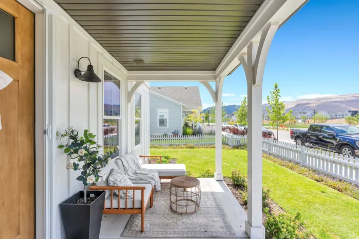 Covered front porch featuring a wood-finish entry door, white board and batten siding, decorative white columns, and a dark corrugated ceiling