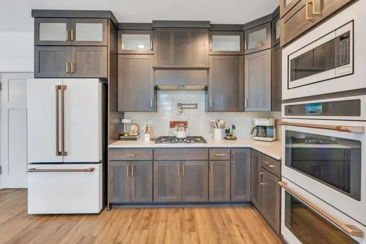 Gourmet kitchen featuring custom cabinetry, light-toned countertops, professional-grade stainless steel appliances, a built-in range hood, and wood-finish flooring