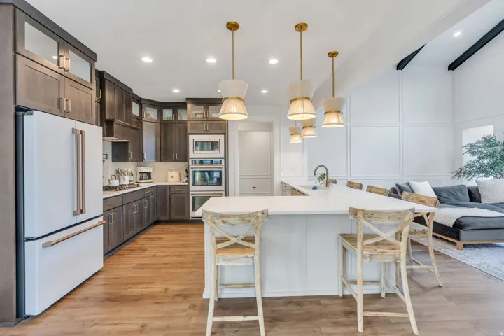 Gourmet kitchen with wood-finish flooring, dark wood cabinetry, integrated double ovens, a central island with countertop seating, and recessed and pendant lighting