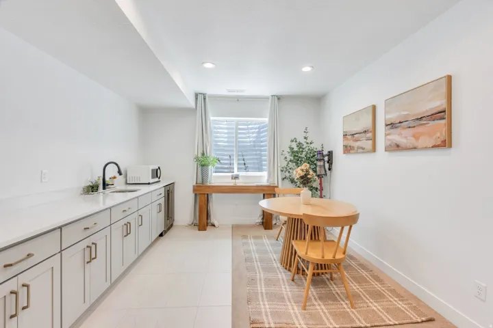 White shaker-style cabinetry with bronze hardware, a built-in beverage refrigerator, and a black gooseneck faucet complement the light-toned countertops and tiled flooring