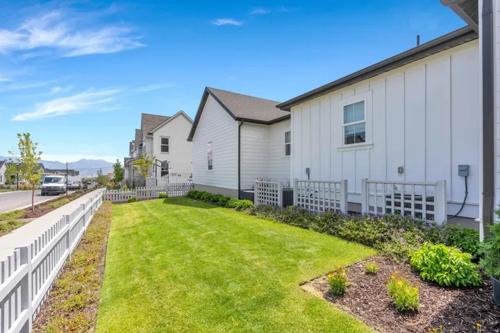 Expansive side yard featuring a manicured lawn, picket fence, and landscaped beds