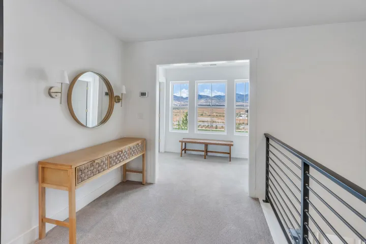 Carpeted hallway leading to a bright space with three large windows offering a mountain and landscape backdrop