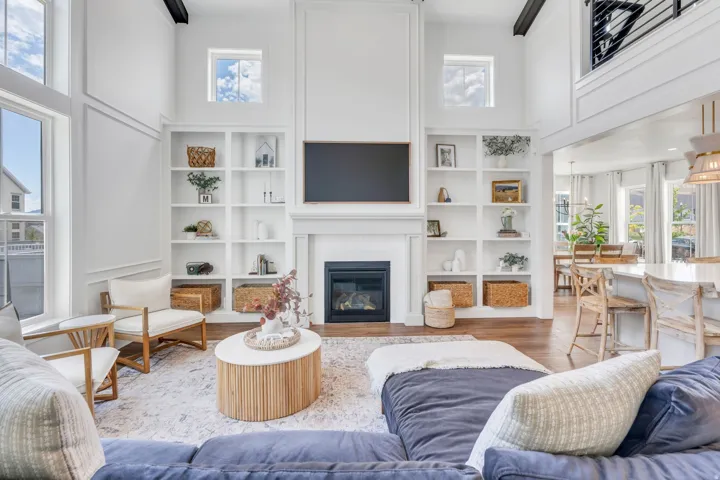 Spacious living area featuring a two-story ceiling, a gas fireplace with a classic mantel, built-in shelving, large windows, and dark wood-finish flooring