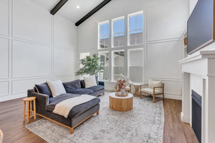 Vaulted ceiling with exposed beams, paneled accent wall, wood-finish flooring, floor-to-ceiling windows, and a built-in fireplace