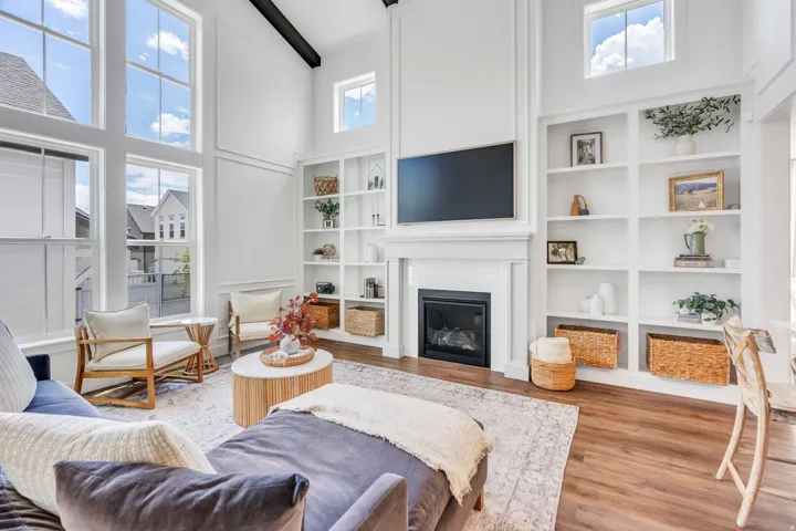 Spacious living area featuring large picture windows, vaulted ceilings with dark-stained beams, a built-in fireplace with a white mantel, extensive built-in shelving, and wood-finish flooring