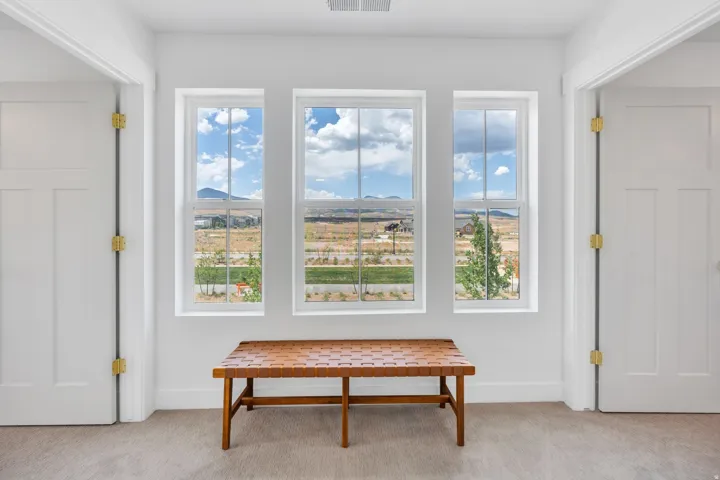 Hallway featuring three vertical windows offering expansive scenery, light gray carpet flooring, and white interior doors with brass-toned hardware