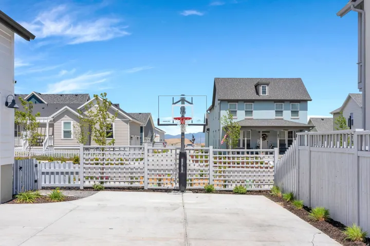Paved concrete driveway featuring a basketball hoop, bordered by a white lattice fence and a solid privacy fence