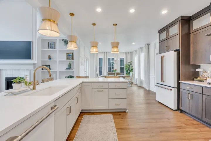 Open-concept kitchen featuring white shaker-style cabinetry, a built-in sink, gold-finish faucet, and pendant lighting