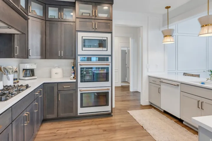 Modern kitchen featuring dark wood-finish cabinetry with glass-front uppers, white countertops, built-in double ovens, and a gas range