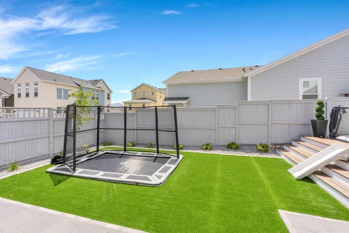 Expansive backyard featuring artificial turf, a light-toned privacy fence, a multi-tiered wood-finish deck, and surrounding gravel landscaping