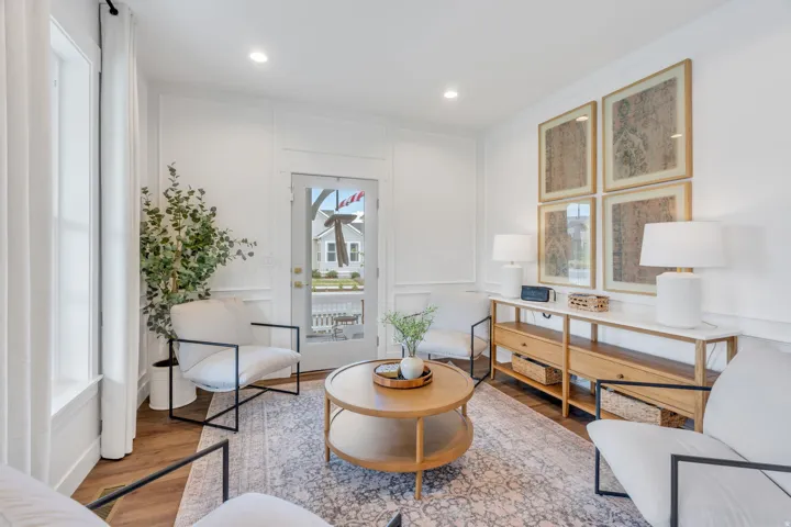 Bright living space featuring wood-finish flooring, white walls with decorative molding, and a glass-paneled door
