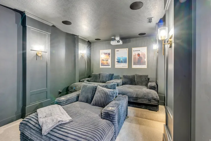 Dedicated media room featuring recessed ceiling speakers, wall-mounted sconces, and a ceiling-mounted projector