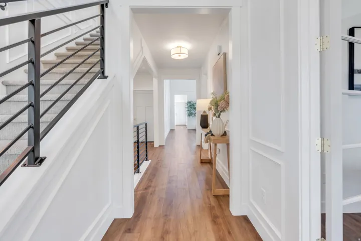 Hallway featuring wood-finish flooring, white panel molding, and a staircase with black metal balusters and carpeted treads