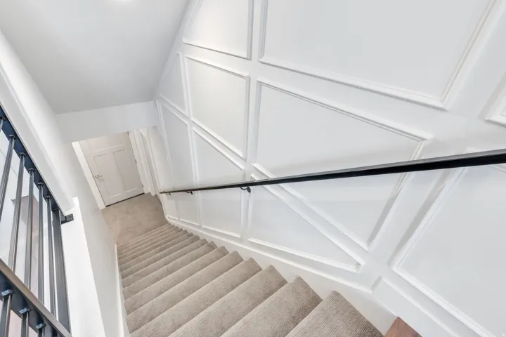 Stairwell featuring wainscoting paneling, a carpeted staircase, a black metal handrail, and white paneled doors