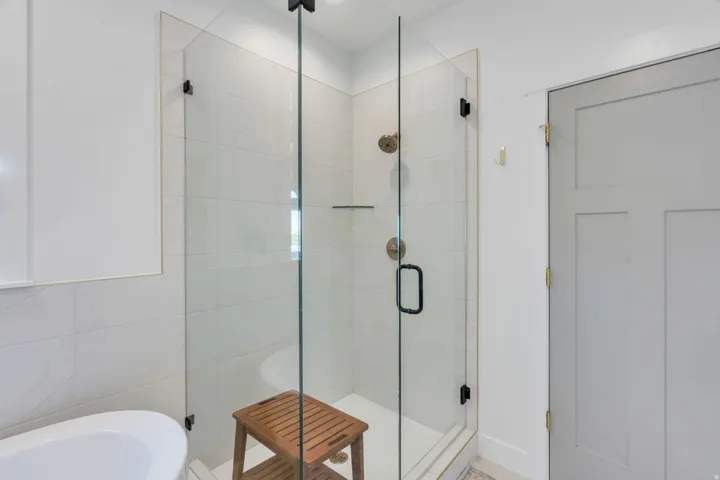 Glass-enclosed shower with white tiled walls, dual shower heads, and an integrated shelf