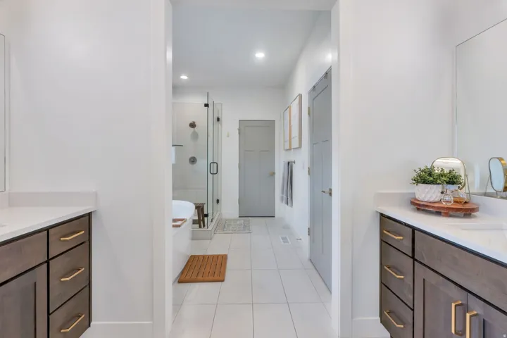 Contemporary bathroom featuring dual wood-finish vanities with light countertops, individual mirrors, and gold-tone hardware