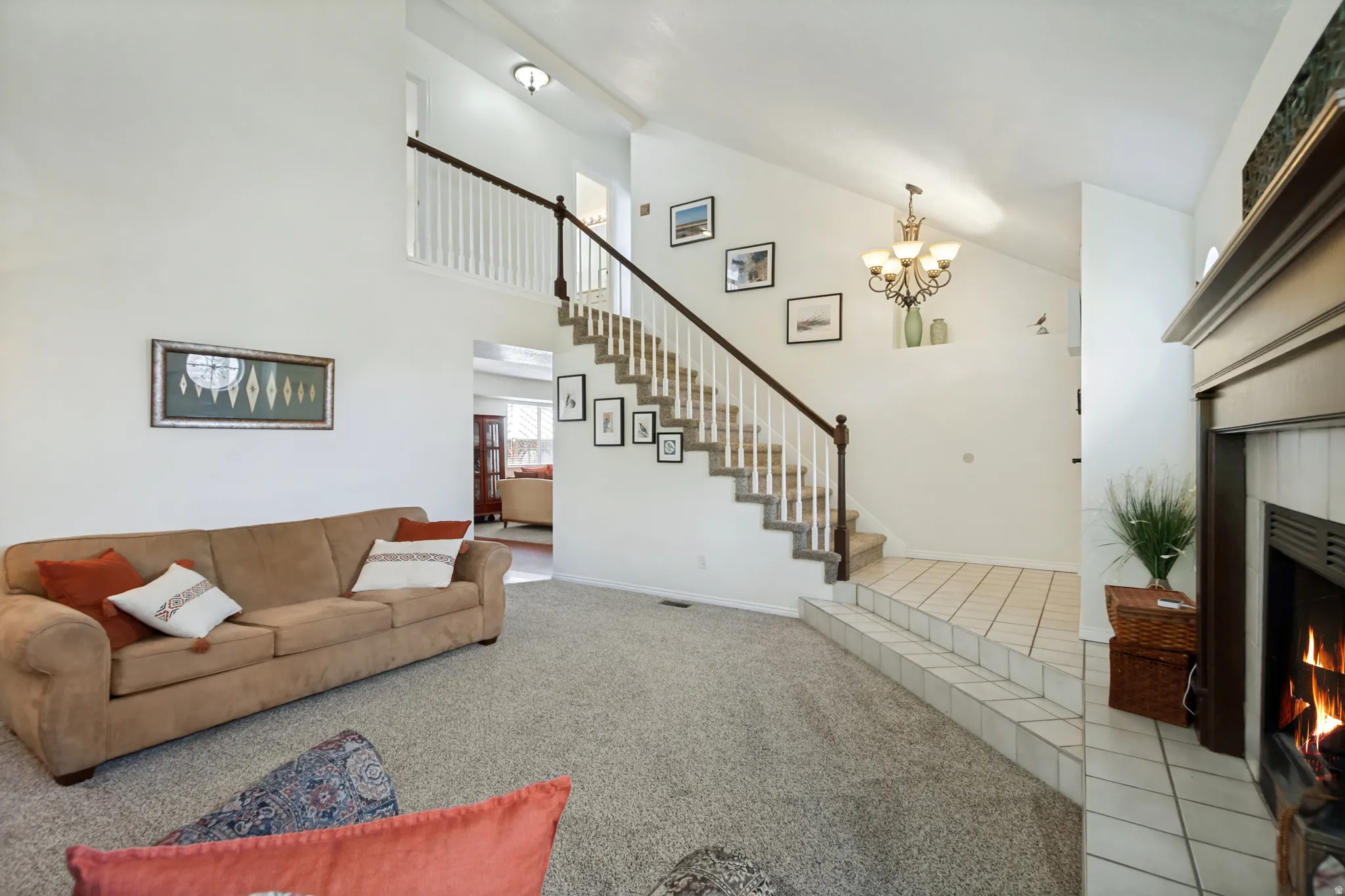 Living area featuring a fireplace with a wood-finish mantel, carpeted flooring, and a two-story ceiling