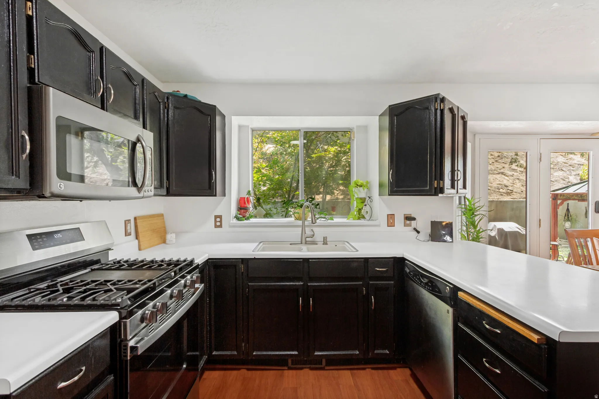 Kitchen featuring dark wood cabinetry, white countertops, stainless steel appliances, a gas range, and wood-finish flooring