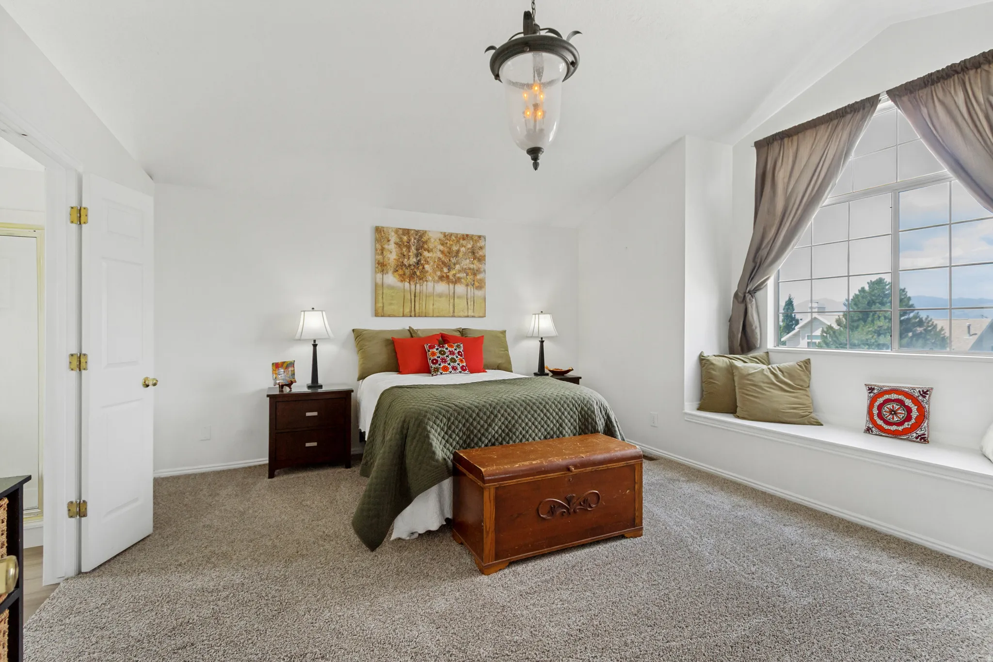 Carpeted room featuring a large window with a built-in window seat, vaulted ceiling, and an overhead light fixture