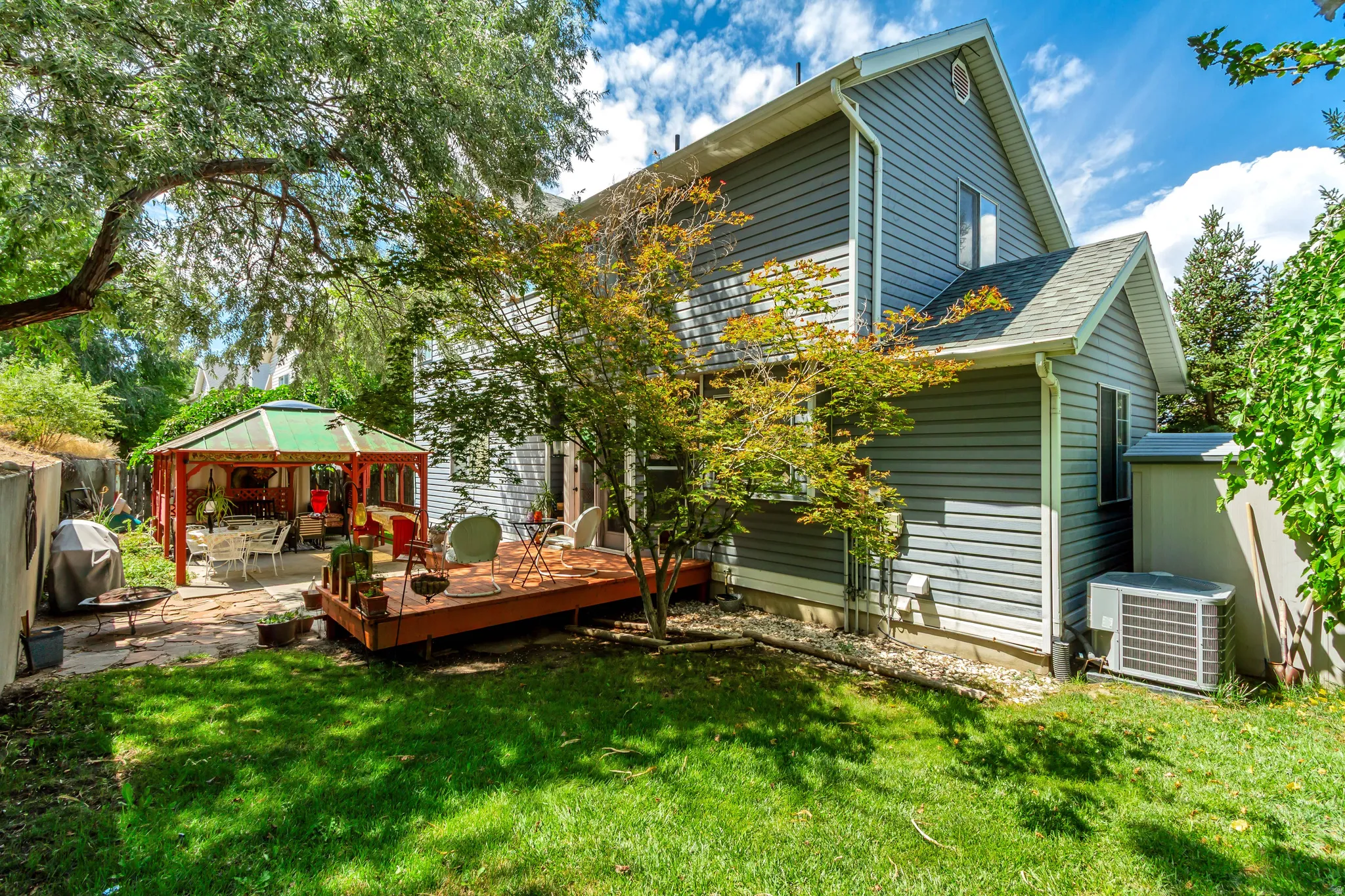 Expansive backyard featuring a stone patio, a wooden deck, and a green-roofed gazebo