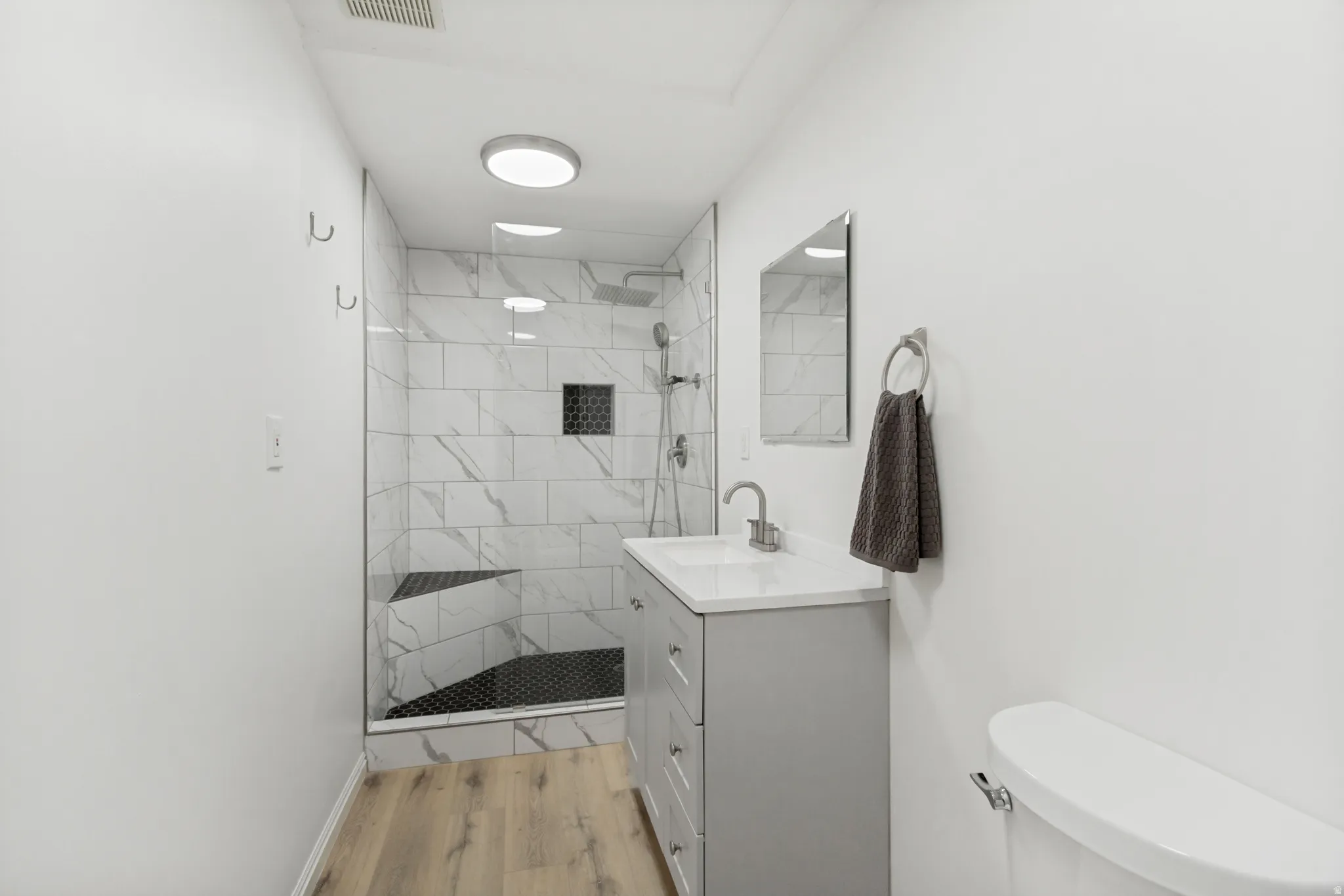 Bathroom featuring a glass-enclosed shower with white marble-look subway tile, a built-in shower bench, and dark hexagonal floor tile