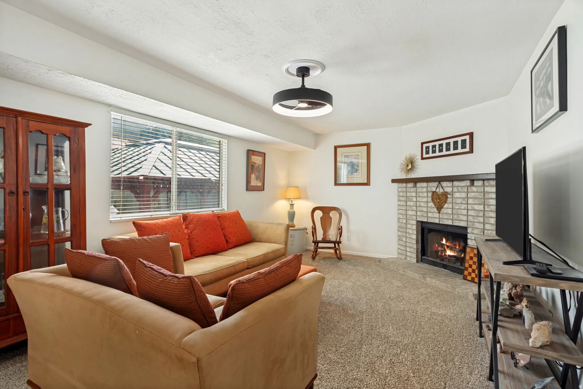 Living area featuring a brick-surround fireplace, wall-to-wall carpeting, a window with blinds, and a contemporary ceiling light fixture