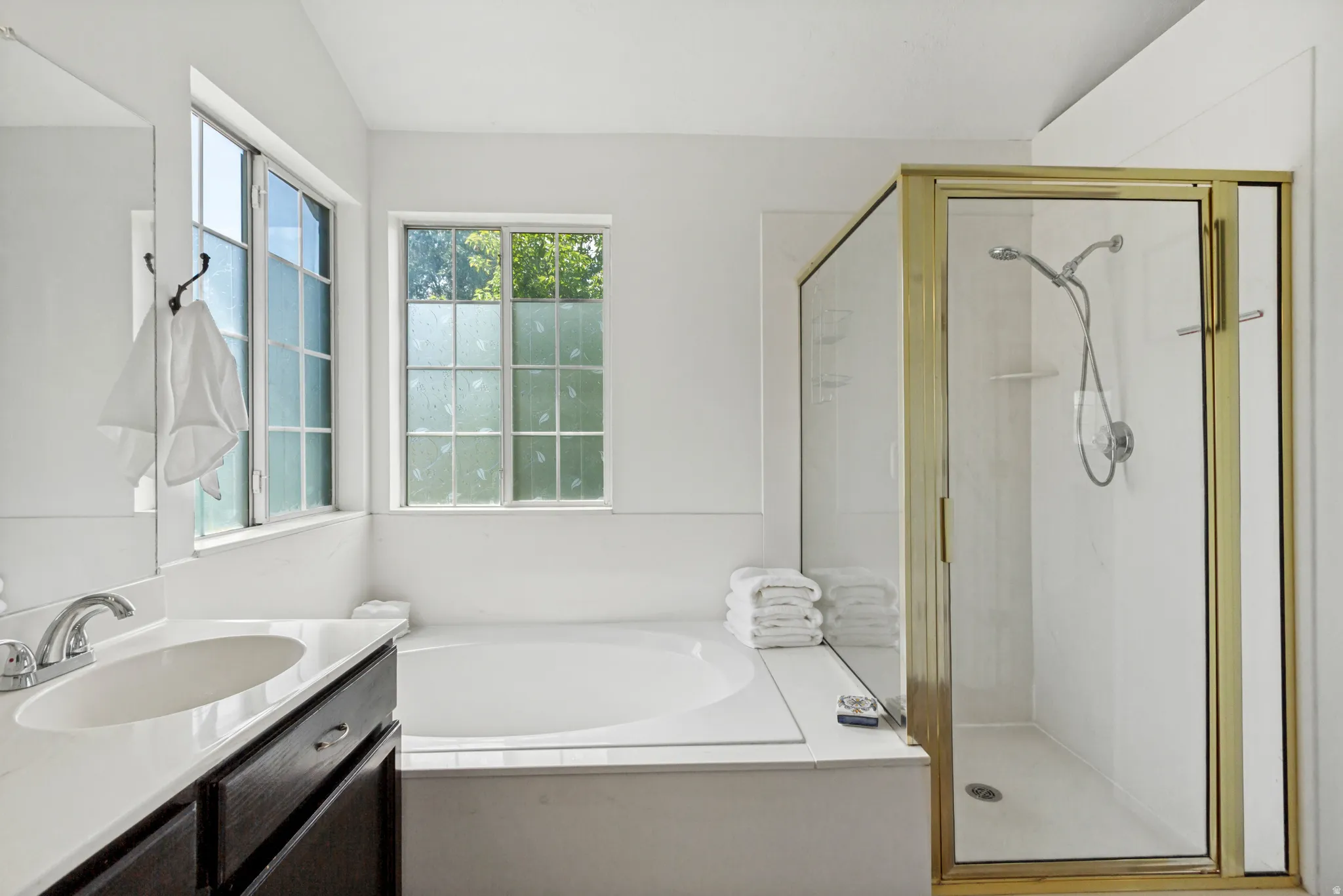 Bathroom featuring a built-in soaking tub, separate glass-enclosed shower with gold-tone framing, and a vanity with an integrated sink and white countertop