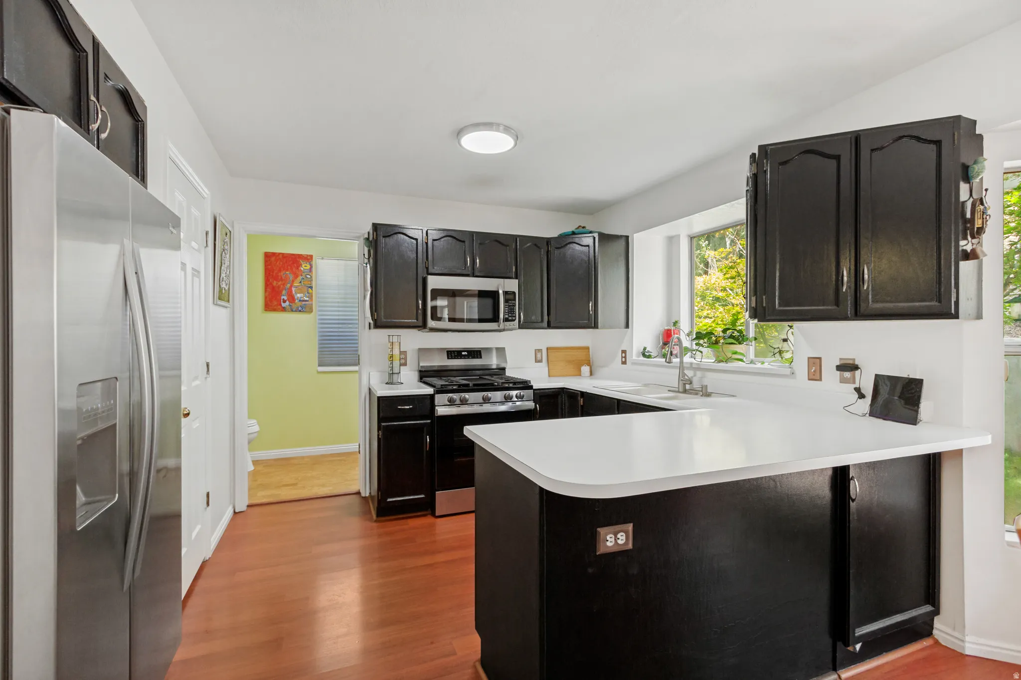 Kitchen featuring black cabinetry, stainless steel appliances, white countertops, and wood-finish flooring