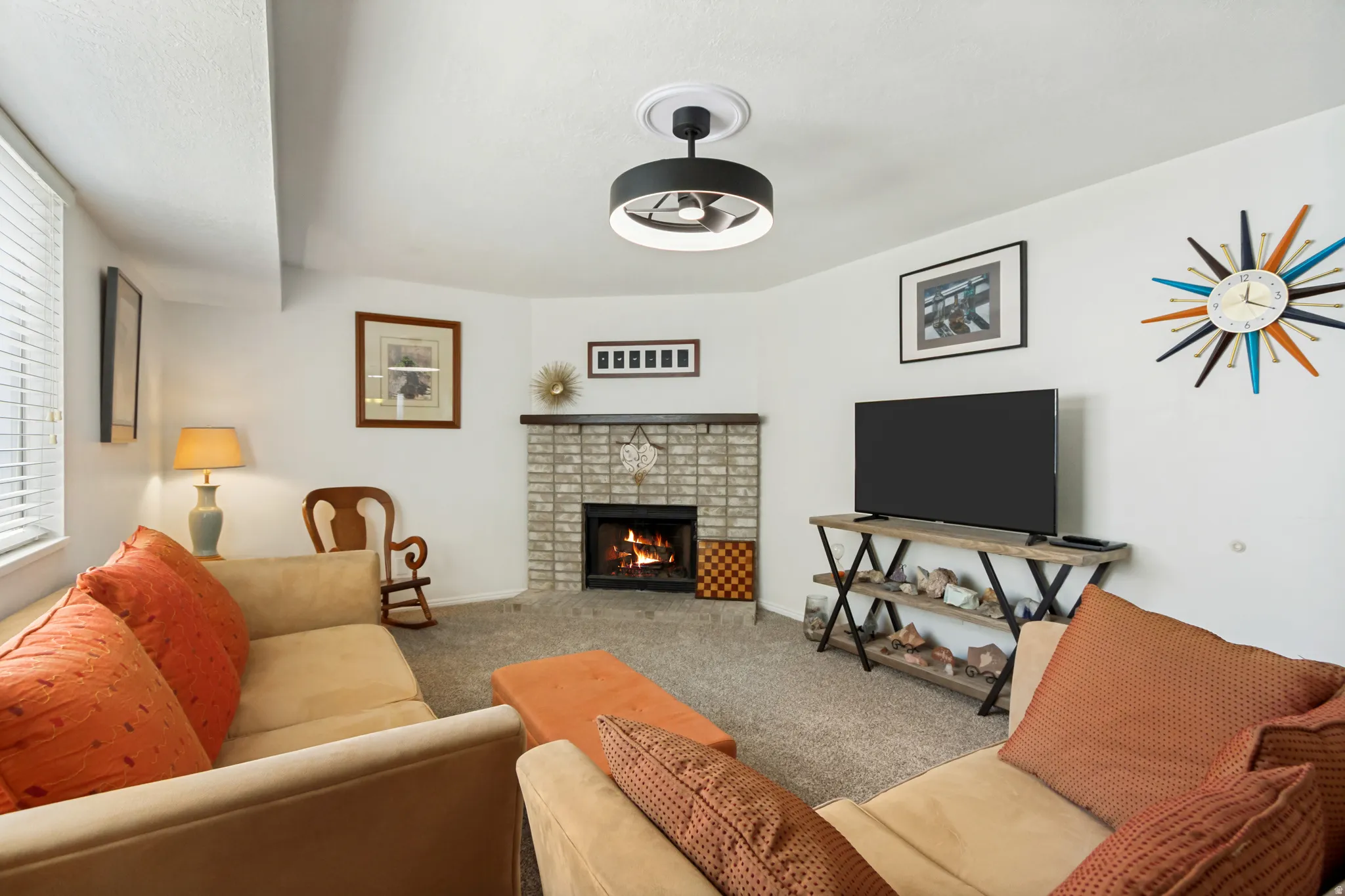 Living space with a corner fireplace featuring light-colored brick surround and dark wood mantel