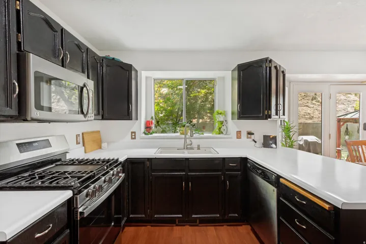 Kitchen featuring dark wood cabinetry, white countertops, stainless steel appliances, a gas range, and wood-finish flooring