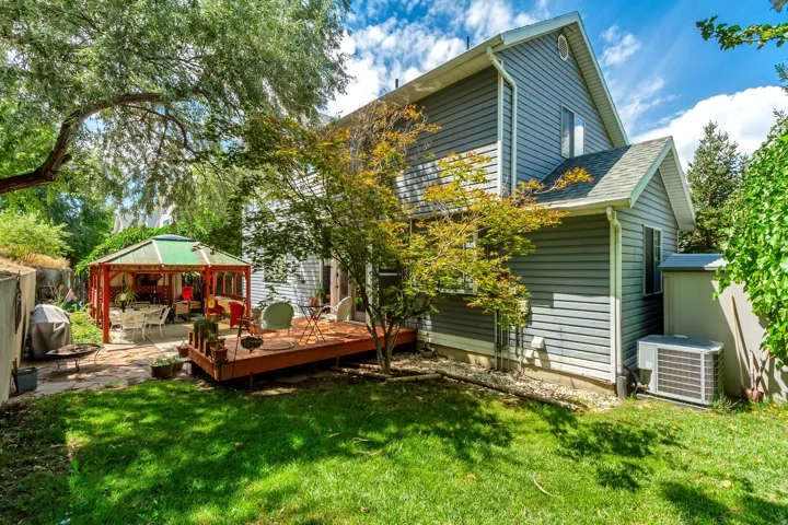 Expansive backyard featuring a stone patio, a wooden deck, and a green-roofed gazebo