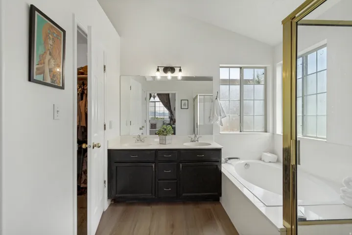 Bathroom featuring a dual vanity with dark wood cabinetry and light countertops, a built-in soaking tub, and a separate shower with a gold-toned frame