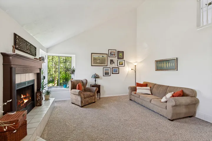Cathedral ceiling living space with a fireplace featuring a dark wood mantel and a tiled hearth