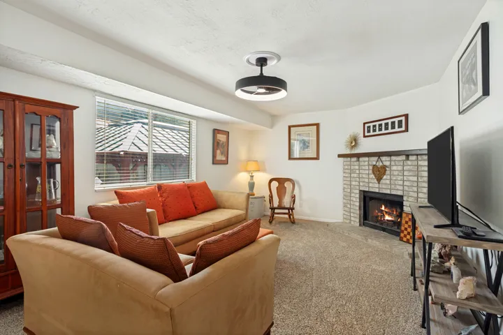 Living area featuring a brick-surround fireplace, wall-to-wall carpeting, a window with blinds, and a contemporary ceiling light fixture