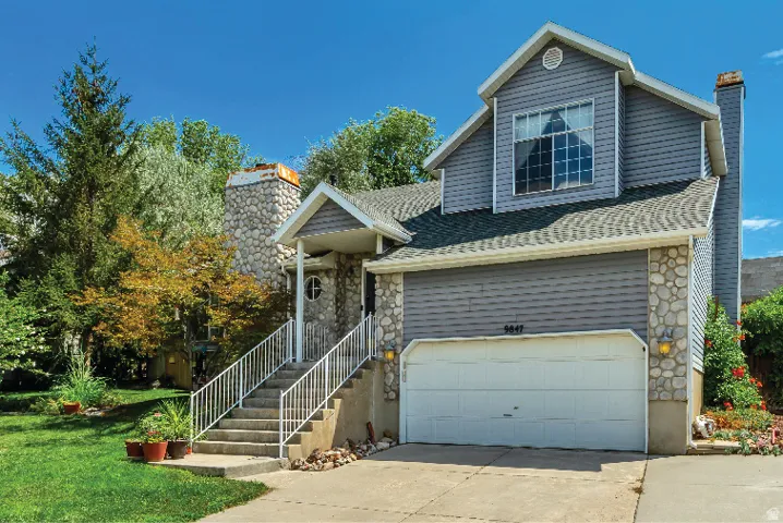 Exterior featuring a combination of stone veneer and horizontal siding, an attached garage, a prominent stone chimney, a front entrance with a covered porch and concrete steps, and established landscaping with mature trees