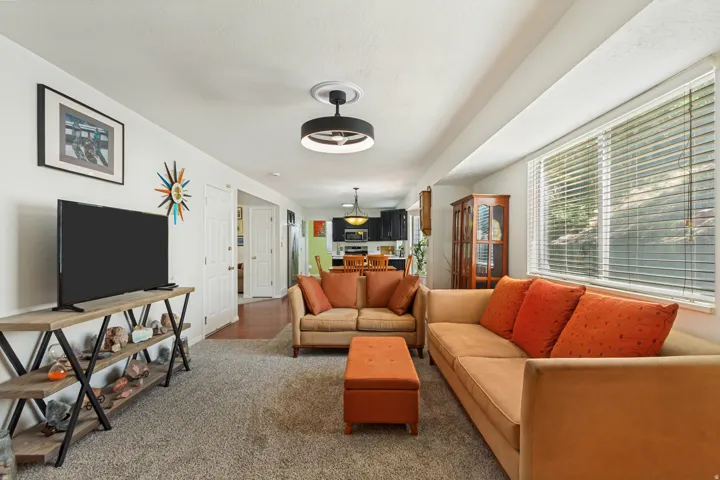 Spacious living area featuring neutral carpet flooring, a large window with horizontal blinds, and a contemporary ceiling light fixture