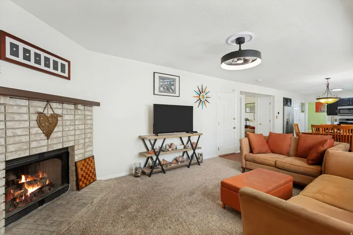 Living area featuring a brick-faced fireplace with hearth, a ceiling fan with integrated lighting, and carpeted flooring