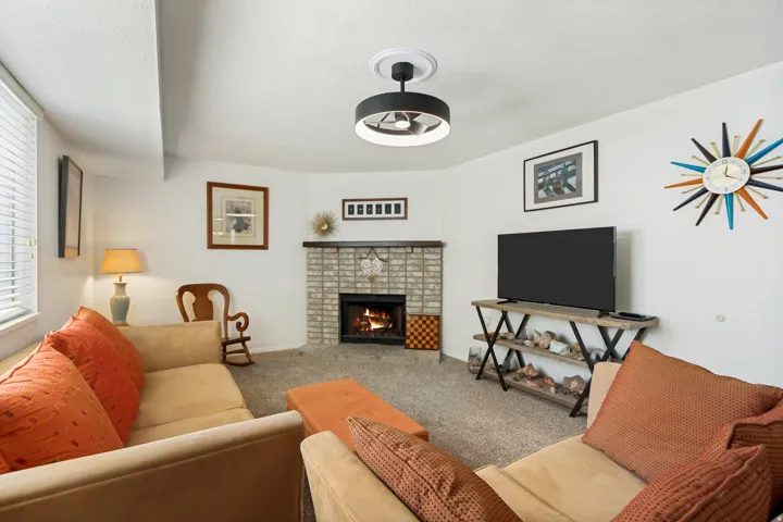 Living space with a corner fireplace featuring light-colored brick surround and dark wood mantel