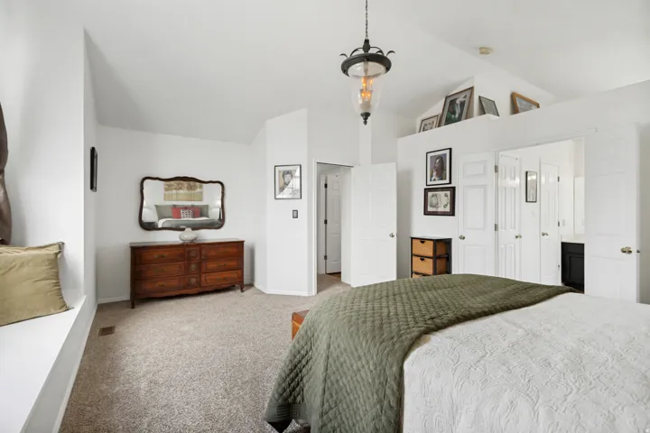 Spacious bedroom featuring vaulted ceilings, a window bench, and light-colored carpeting