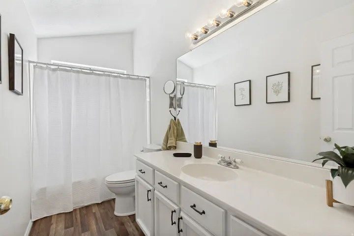 Bathroom featuring a white vanity with a single basin sink, wood-finish flooring, and a tub with shower