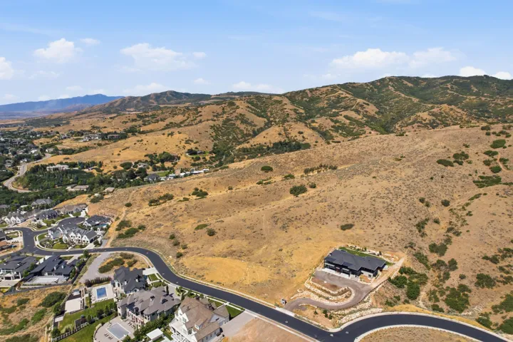 Expansive undeveloped lot featuring a paved road frontage, natural hillside terrain, and distant mountain scenery