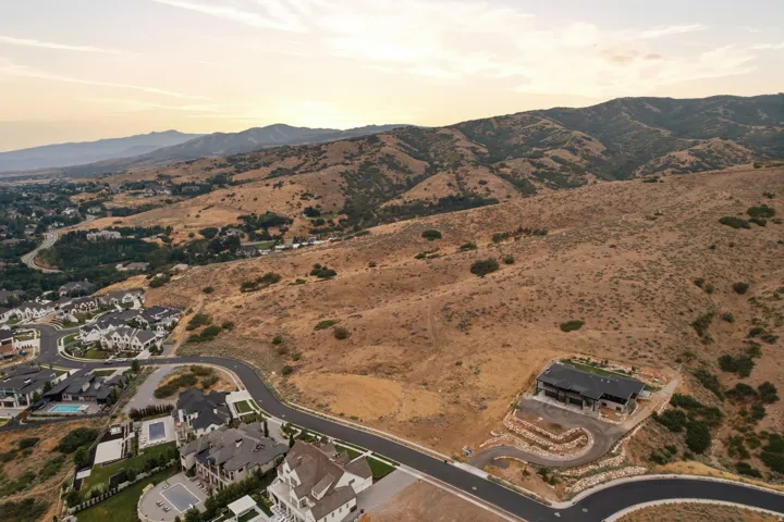 Expansive hillside property featuring a partially constructed structure, winding paved driveway, terraced landscaping, and sweeping mountain scenery