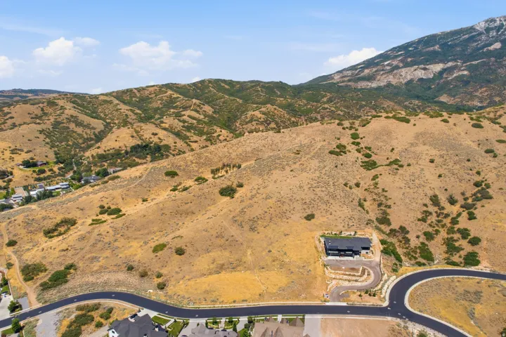 Modern residence situated on a sloped lot, featuring a dark exterior and a paved circular drive
