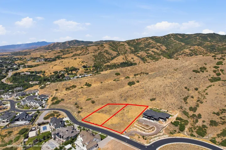 Expansive undeveloped land parcel featuring a paved road frontage, established infrastructure including existing homes, and a mountainous backdrop