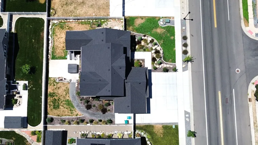Aerial view of a property featuring a dark-shingled roof, a concrete driveway, and an established street