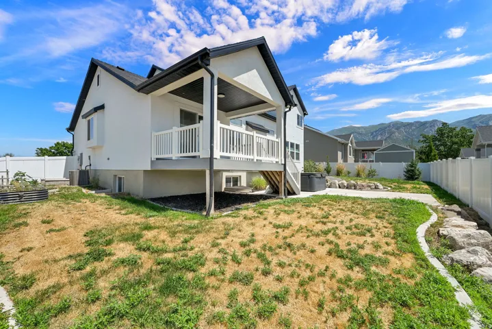 Backyard featuring a covered deck with white railing, concrete patio, and white vinyl fencing