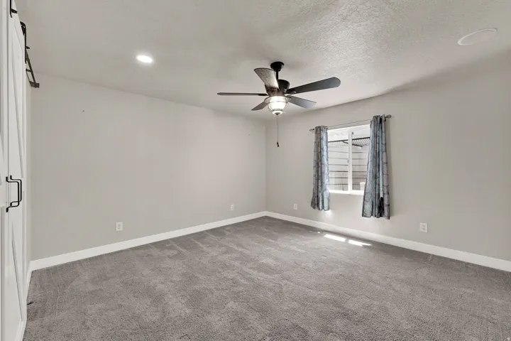 Spacious room featuring neutral carpeting, light-colored walls, and a ceiling fan with integrated lighting
