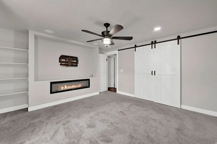 Contemporary linear fireplace with a built-in media niche, custom shelving, and twin sliding barn doors